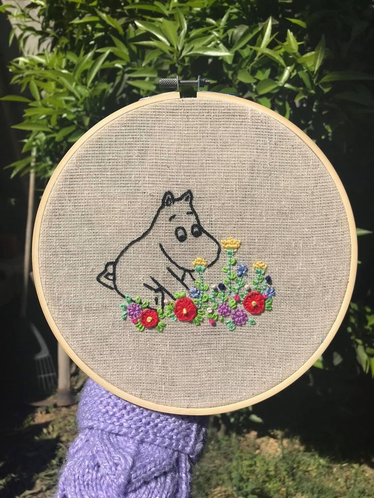 a person holding up a cross - stitch hoop with a drawing of a dog on it