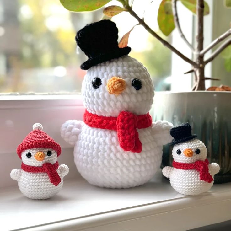 there is a crocheted snowman and two small snowmen on the window sill