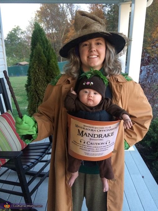 a woman holding a baby wearing a hat and costume on her back while standing in front of a porch