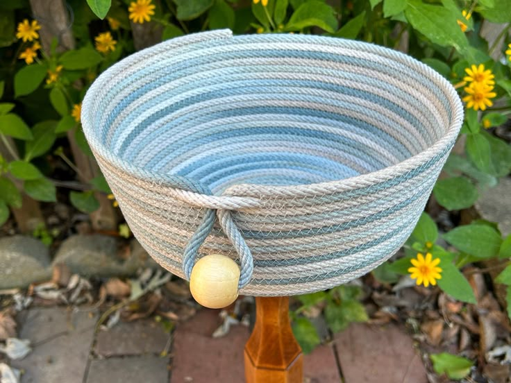 a blue and white basket sitting on top of a wooden stand next to yellow flowers