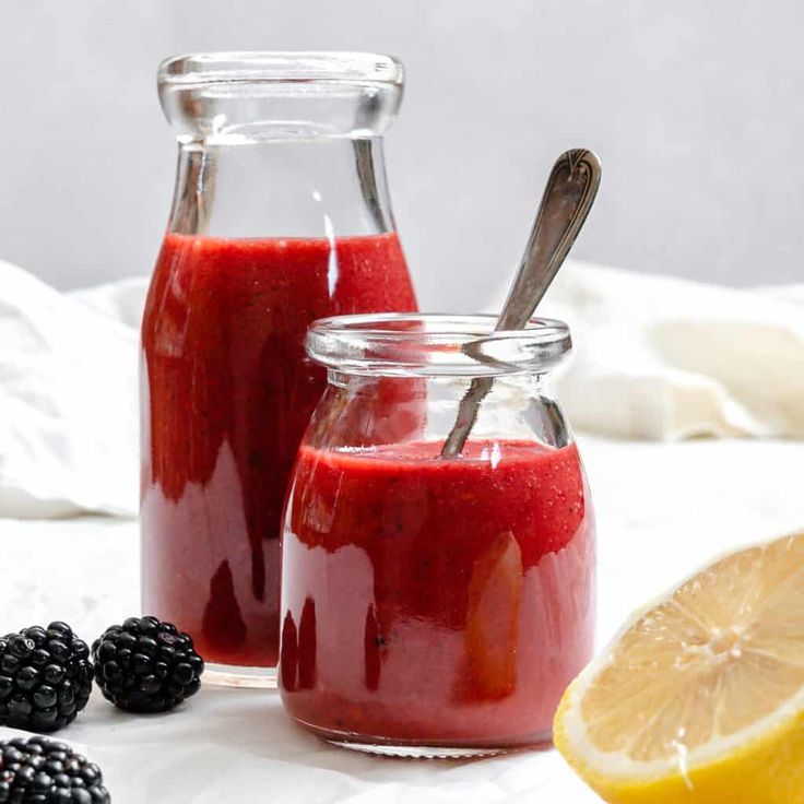 two glass jars filled with raspberry sauce next to lemon slices and blackberries