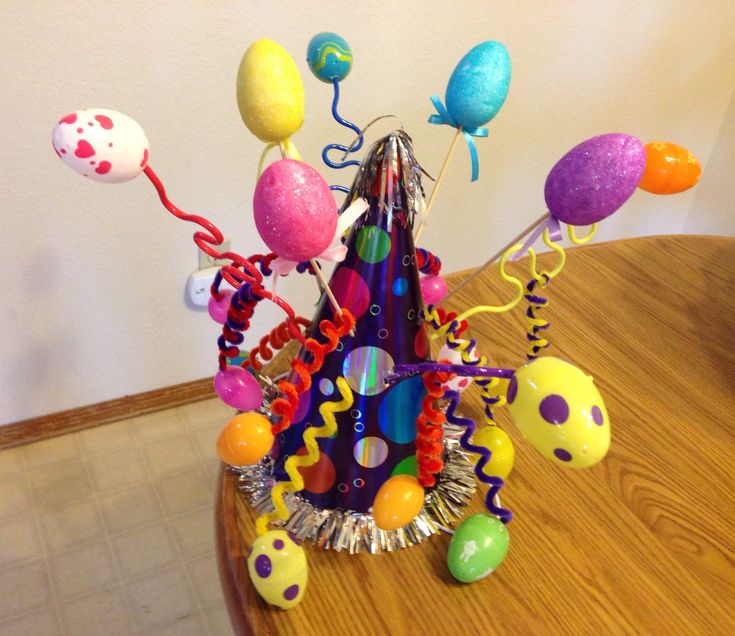 an arrangement of balloons and streamers in a vase on a wooden table with a white wall behind it