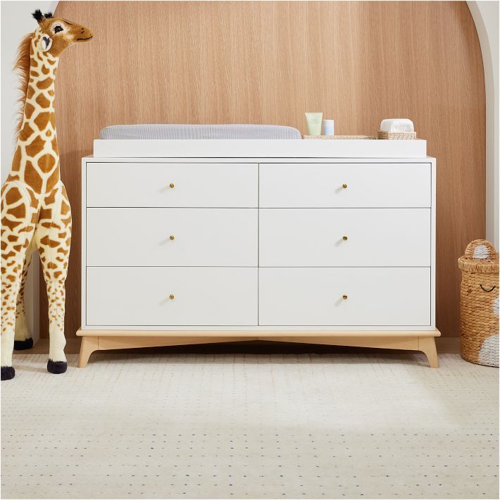 a giraffe standing next to a white dresser