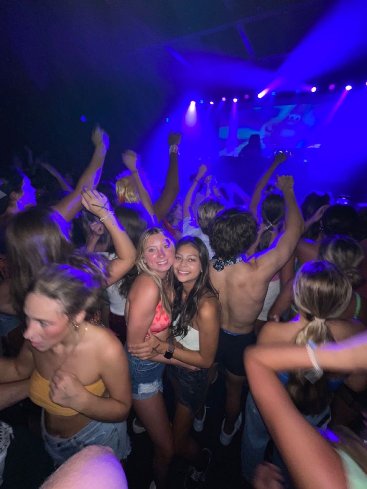 a group of young people dancing at a club or party with their arms in the air