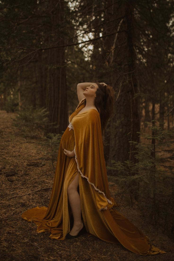 a woman in a yellow dress standing in the woods with her arms behind her head