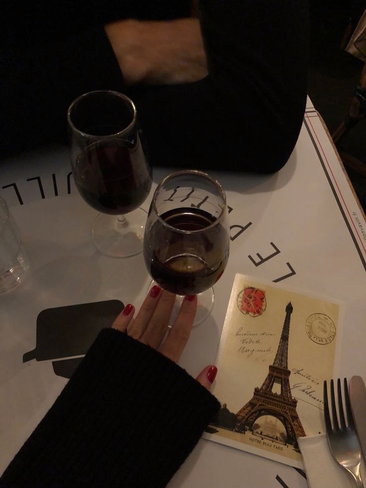 a woman sitting at a table with a glass of wine in front of her and an open book