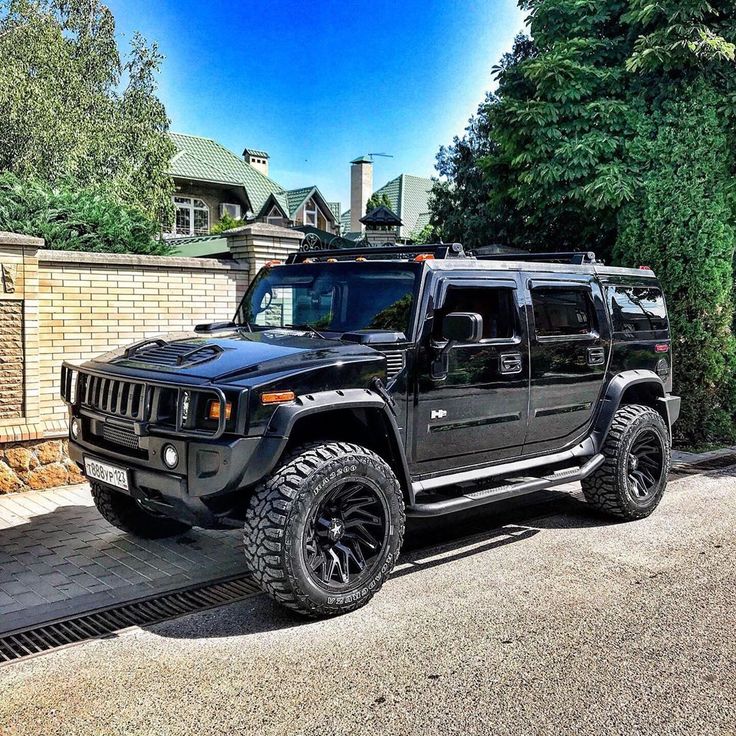 a black hummer truck parked in front of a brick wall and fenced driveway