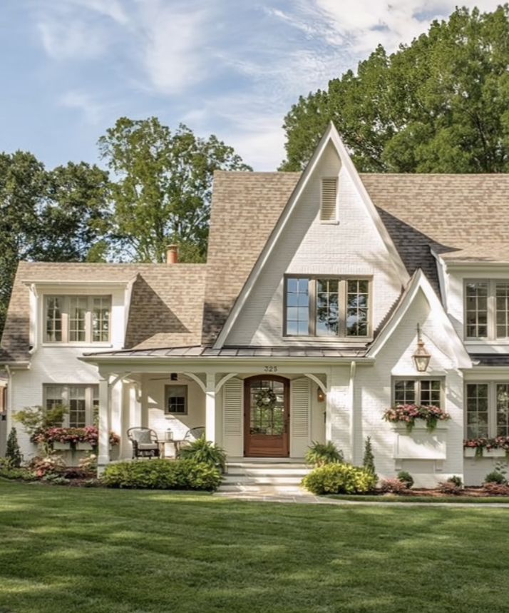 a white house with lots of windows and flowers in the front yard on a sunny day