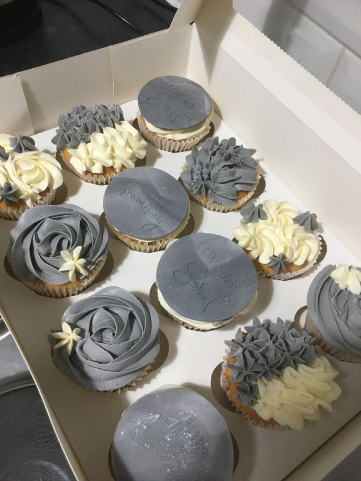 twelve cupcakes in a box with frosting and flowers on the top one