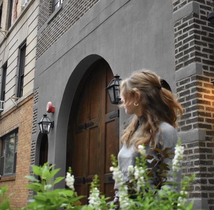 a woman standing in front of a building with flowers growing outside the doors and windows