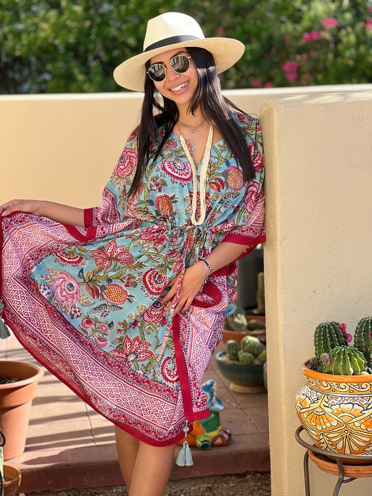 The Bora Bora Botanical Midi Kaftan radiates a refreshing charm with its beautiful blue floral design, complemented by a vibrant red and pink border. This exquisite kaftan features intricate botanical prints that showcase exceptional craftsmanship, blending elegance with a bold splash of color. The flowing silhouette and striking details make it a standout piece, perfect for adding a touch of vibrant sophistication to your wardrobe. 100% cotton voile Length 39" One size fits all with adjustable Red V-neck Kaftan With Vibrant Print, Bohemian Paisley Print Kaftan For Vacation, Traditional Floral Print Summer Kimono, Traditional Summer Kimono With Floral Print, Traditional Floral Print Kimono For Summer, Paisley Print Kaftan For Vacation, Bohemian Kaftan With Floral Print And Kimono Sleeves, Bohemian Kaftan With Paisley Print For Vacation, Blue Floral Print V-neck Kimono