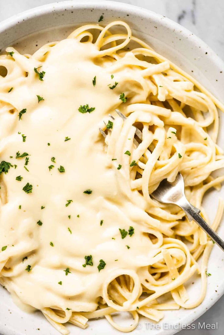 a white bowl filled with pasta covered in cream sauce and parsley on the side