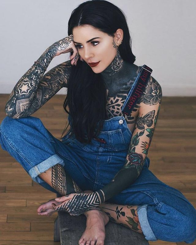 a woman with tattoos on her arms and legs sitting in front of a wooden floor