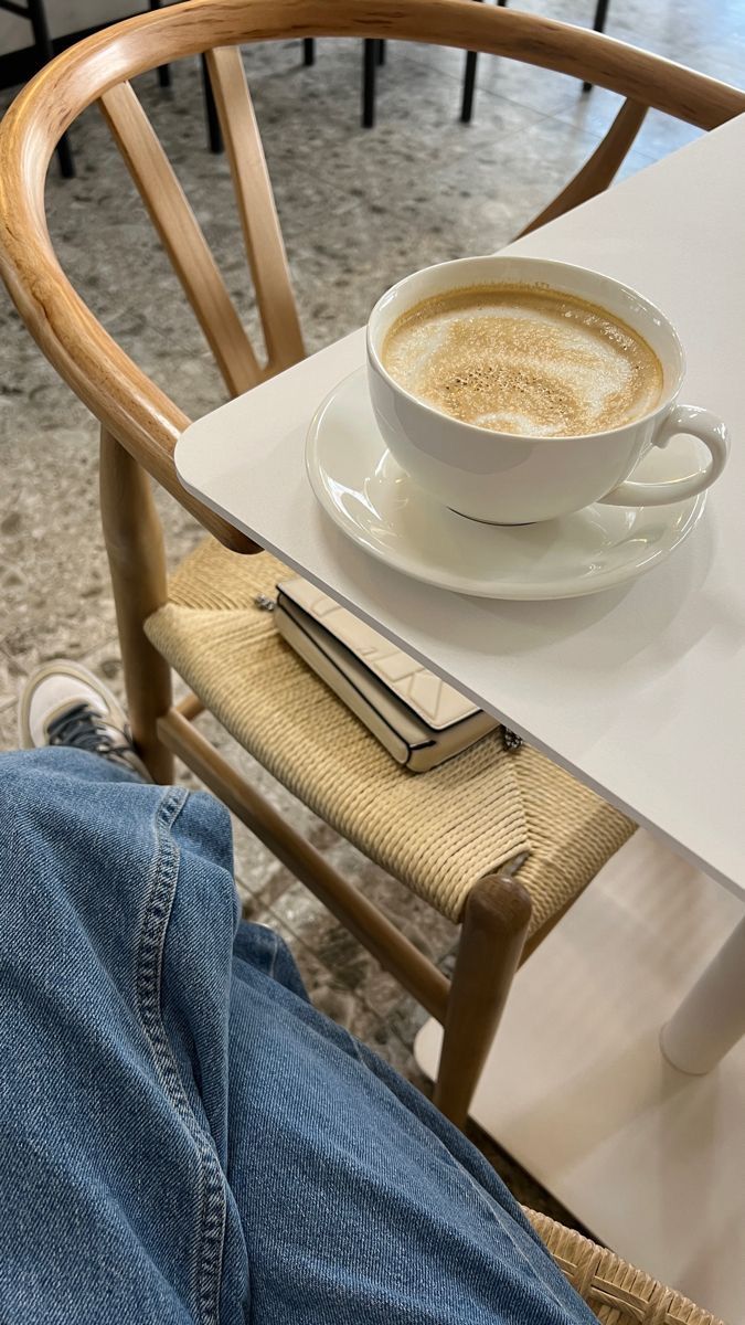 a cup of coffee sitting on top of a white table next to a person's legs