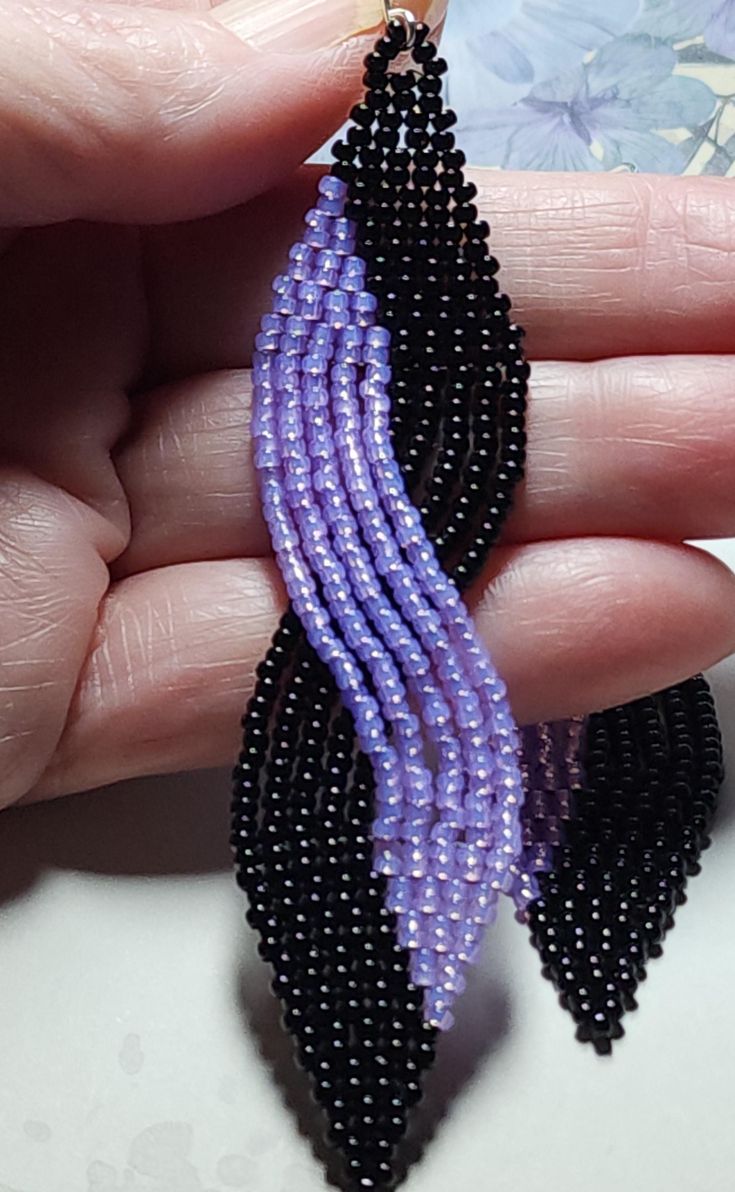 a pair of black and purple beaded earrings on a person's palm hand