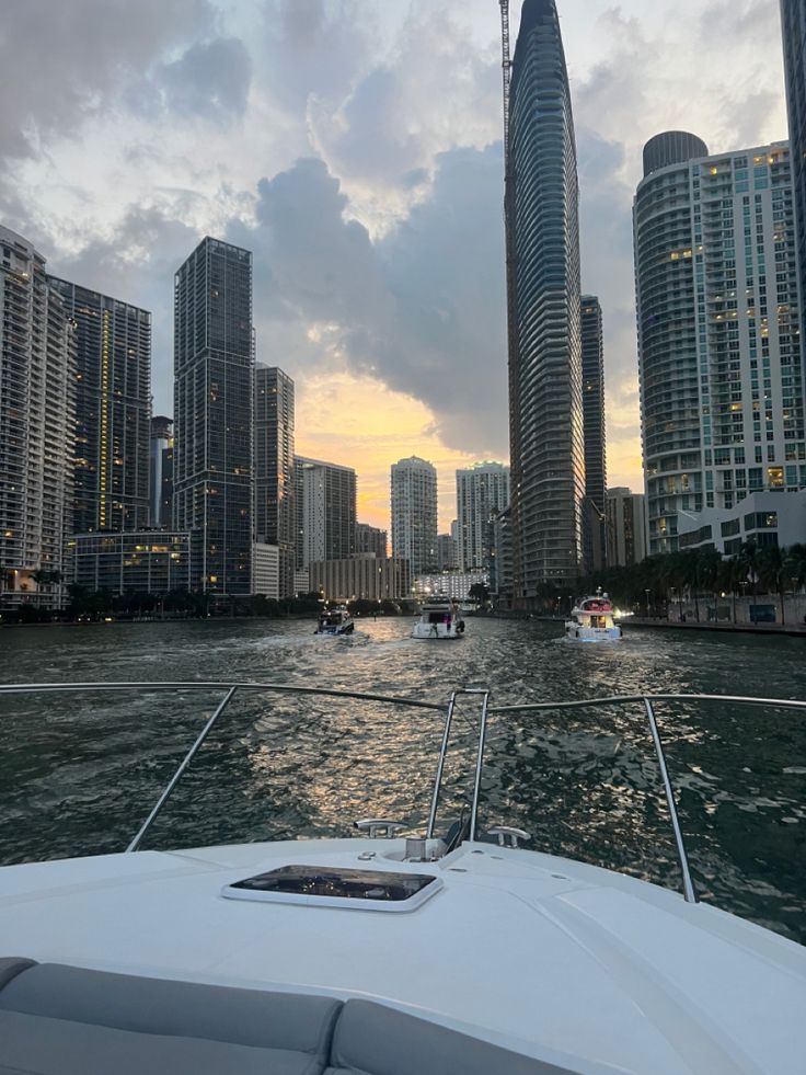 boats are traveling on the water in front of tall buildings and skyscrapers at sunset