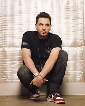 a man sitting on the floor in front of a curtain with his hands clasped to his knees