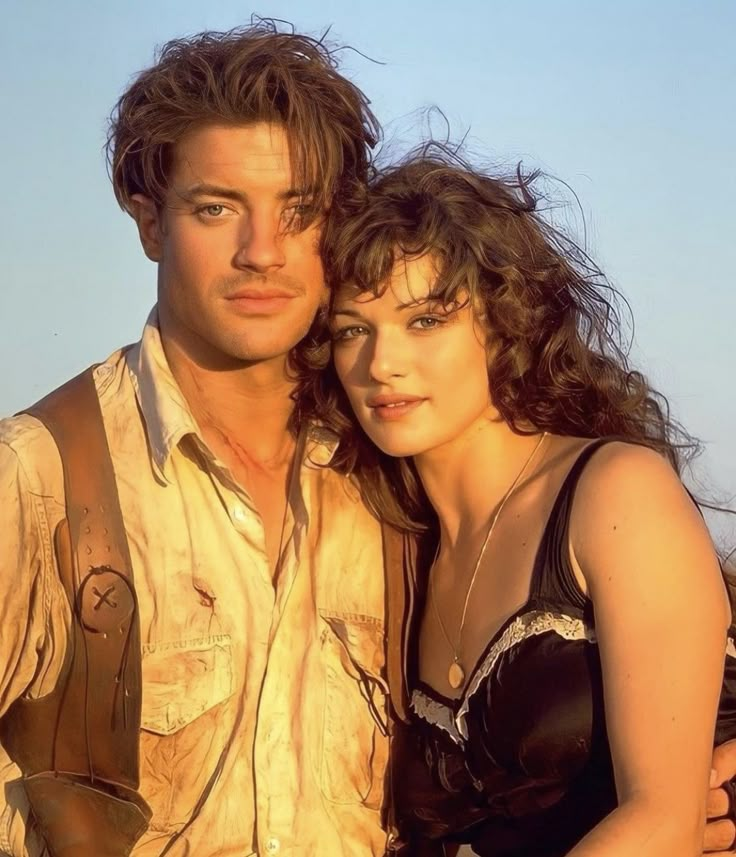 a man and woman standing next to each other on the beach with their arms around each other