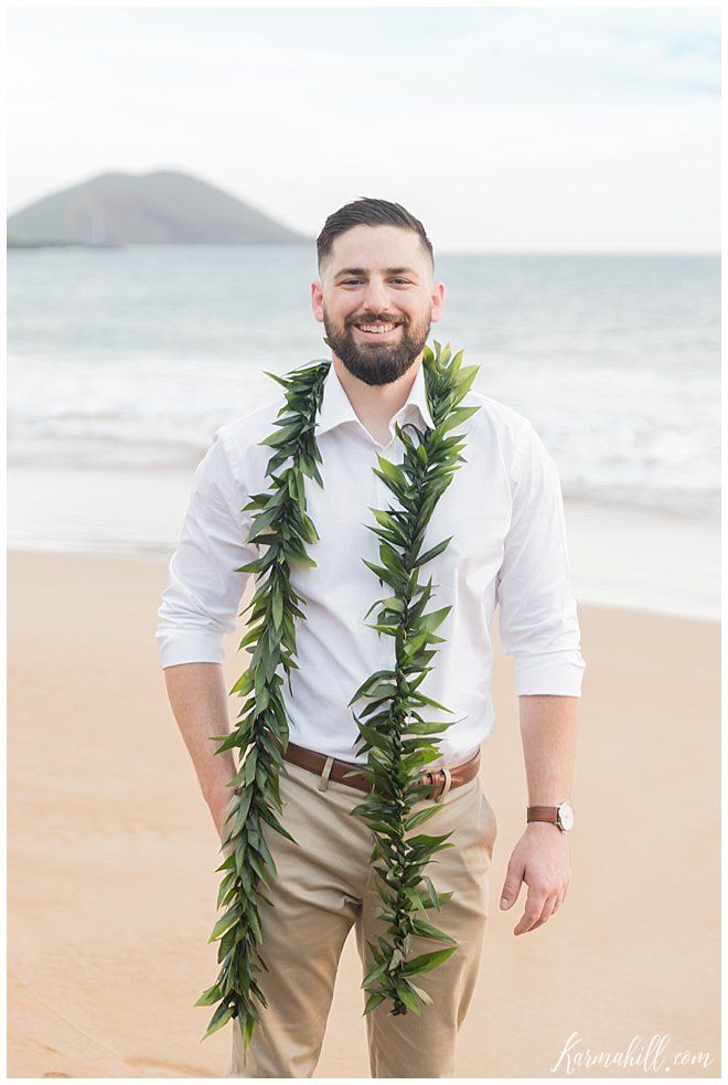 a man standing on top of a sandy beach next to the ocean wearing a lei