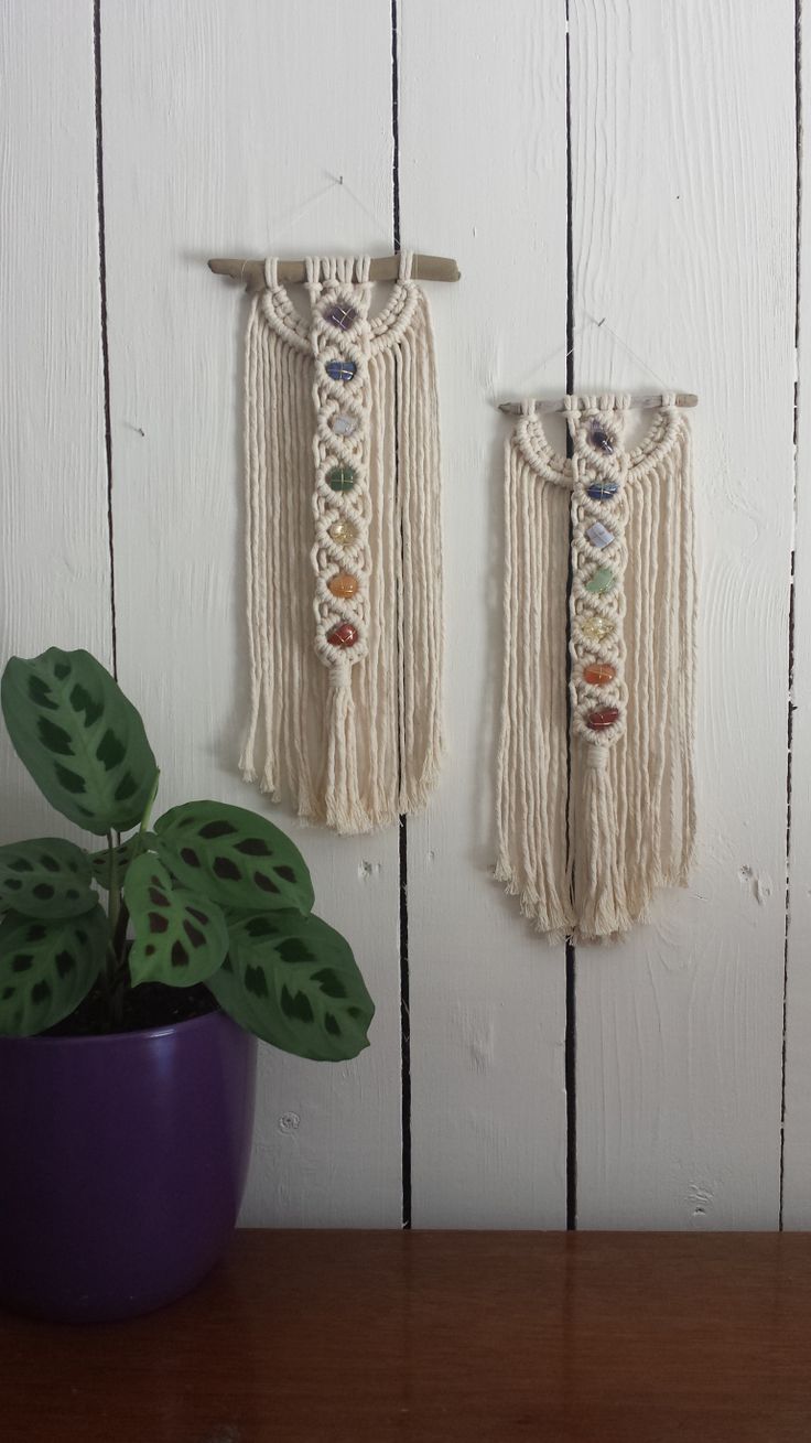 two wall hangings on the side of a white wooden wall with a purple potted plant next to them