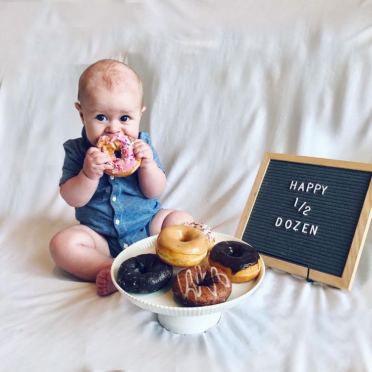 a baby sitting in front of a plate of doughnuts and a sign that says happy v's dozen