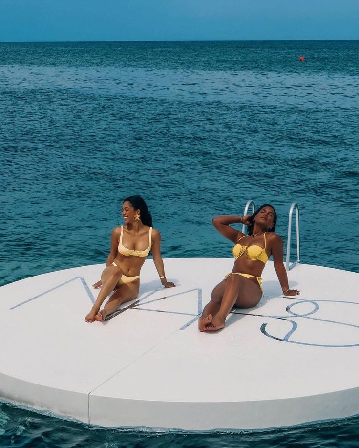 two women in bikinis sitting on the back of a boat