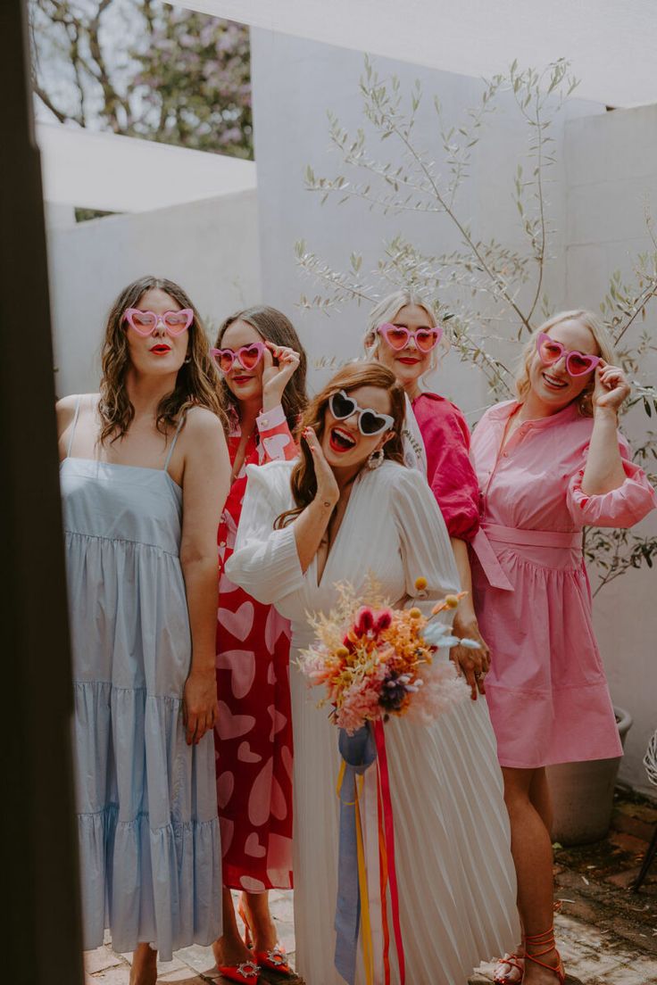 a group of women standing next to each other in front of a white wall wearing sunglasses