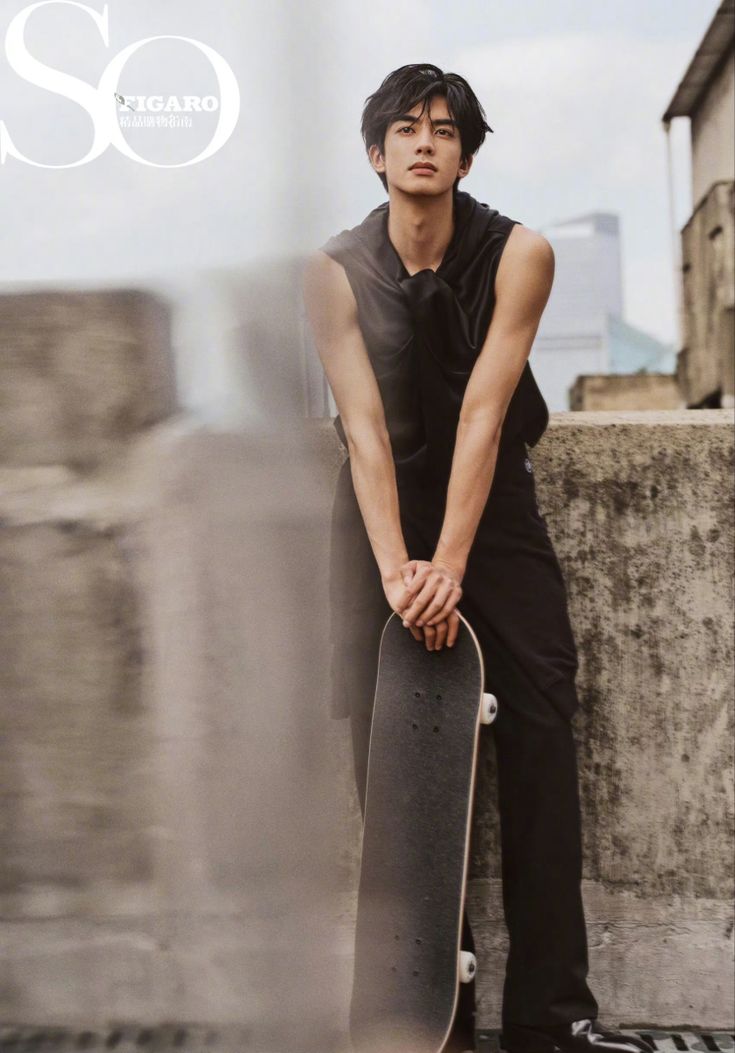 a young man leaning against a wall holding a skateboard