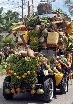 an old jeep is loaded with bananas and other fruits on the back as it drives down the street