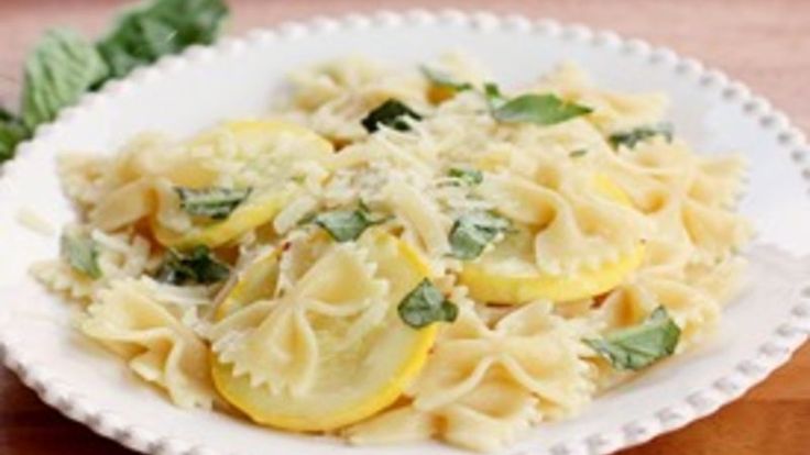 a white bowl filled with pasta and spinach on top of a wooden table next to green leaves