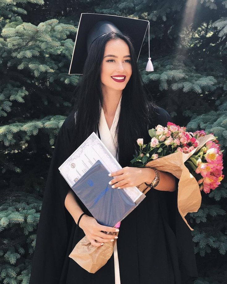 a woman wearing a graduation cap and gown with flowers in her hand holding a book