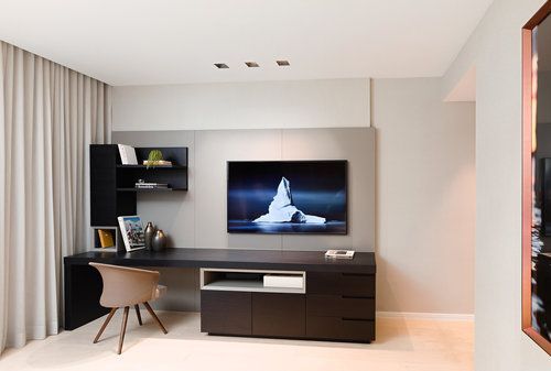 a room with a desk, chair and television on the wall next to a window