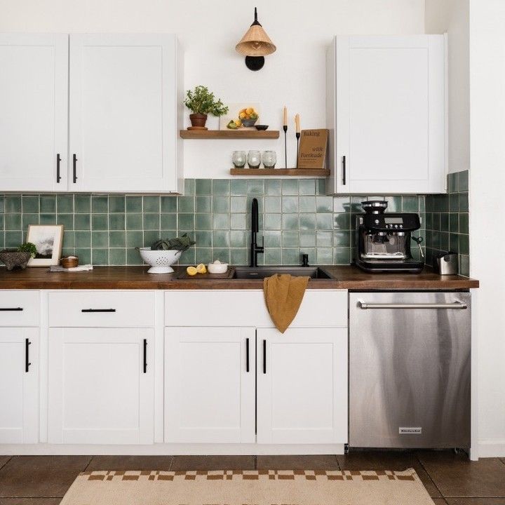 a kitchen with white cabinets and green tiled backsplash