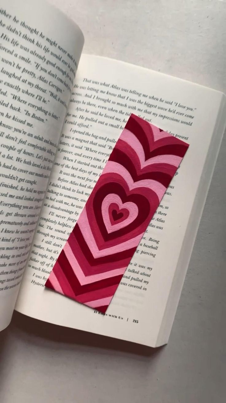 an open book with paper cut into the shape of a heart on top of it