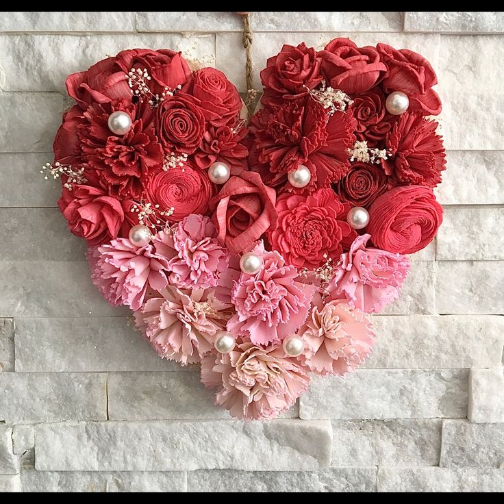 a heart - shaped arrangement of red and pink flowers on a white brick wall with pearls