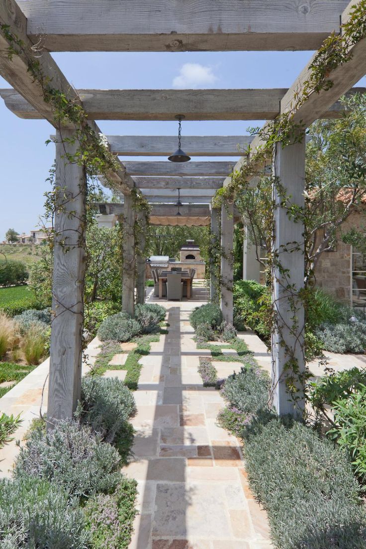 an outdoor garden with stone walkway and pergolated area, surrounded by greenery