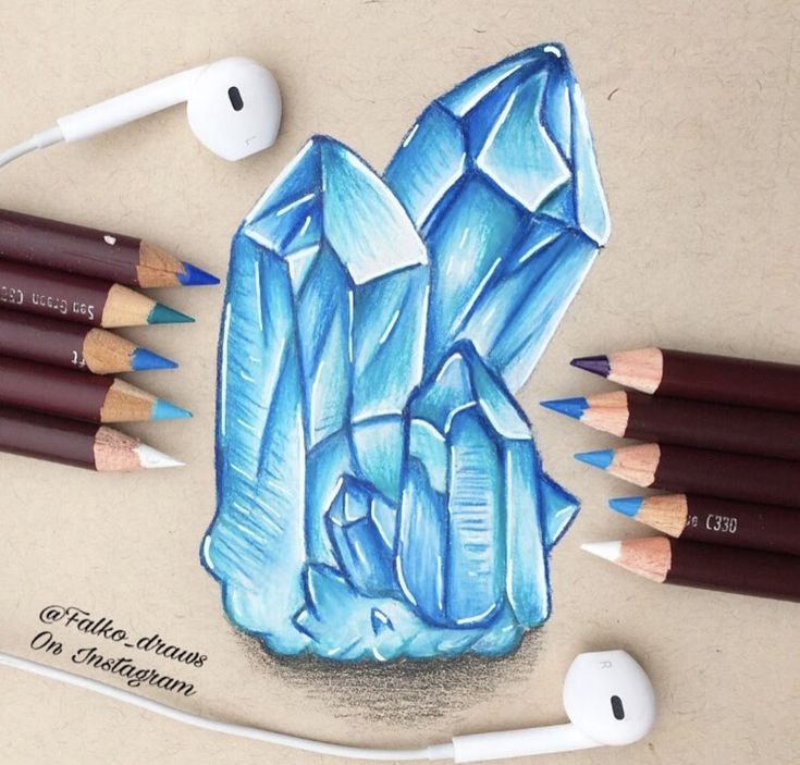 colored pencils and crayons are arranged around a drawing of a blue crystal