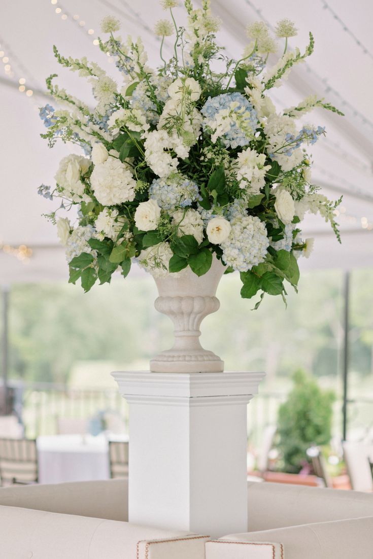 a vase filled with white and blue flowers sitting on top of a table under a tent