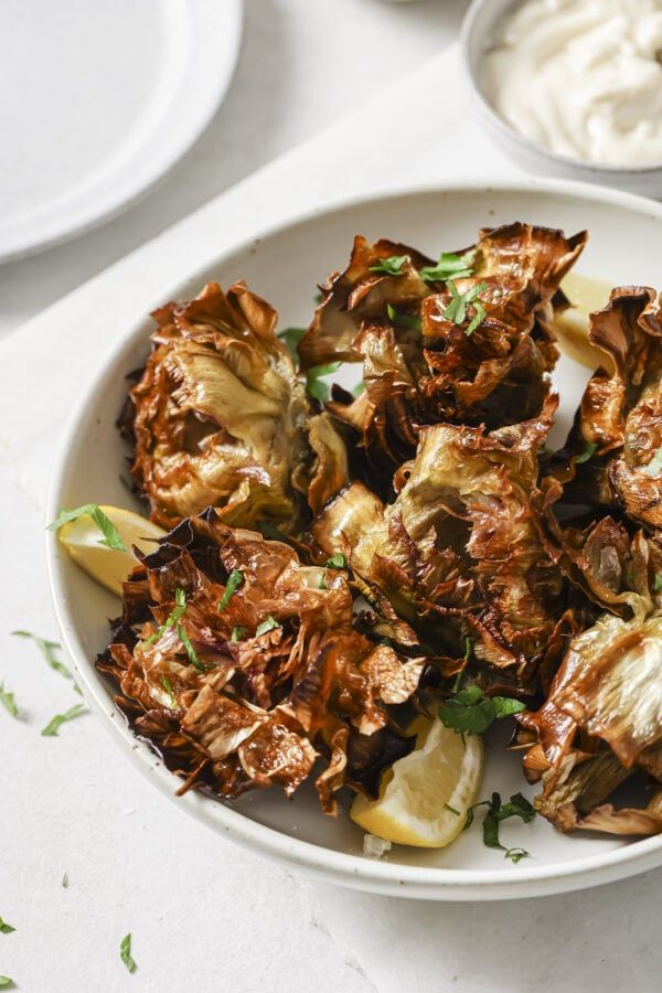 a white bowl filled with cooked artichokes next to some sour cream sauce