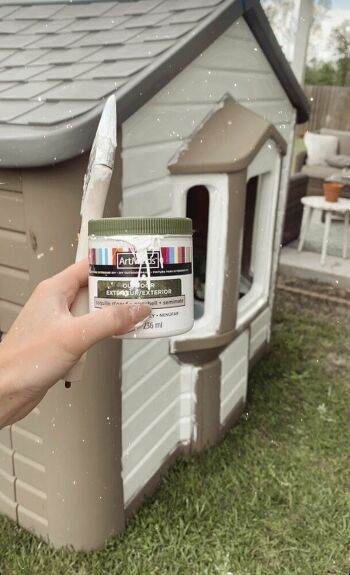 a person holding a paint can in front of a dog house