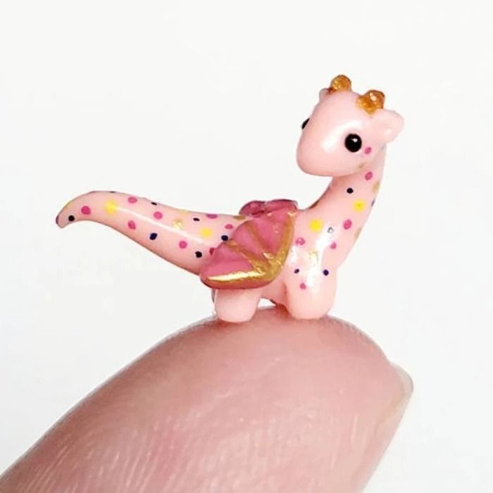 a tiny pink giraffe figurine sitting on top of someone's finger