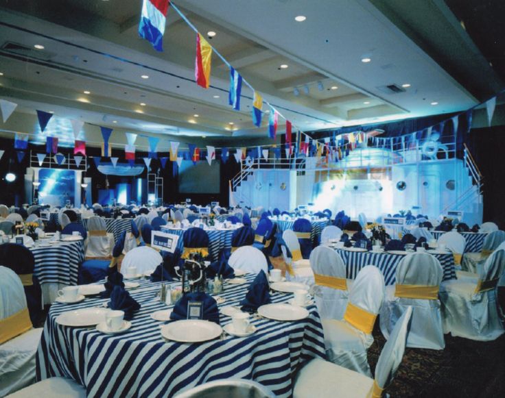 a banquet hall with tables and chairs covered in blue and white striped cloths, decorated with flags