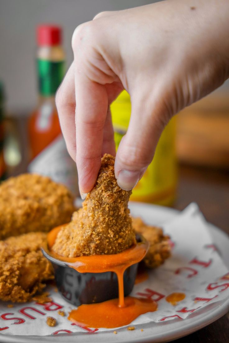 a person dipping something into some kind of sauce on top of chicken nuggies