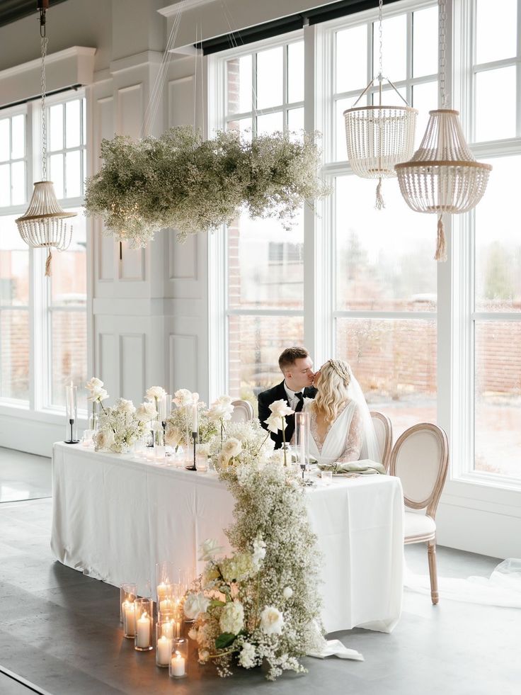 a bride and groom kissing at their wedding table with candles in front of the windows