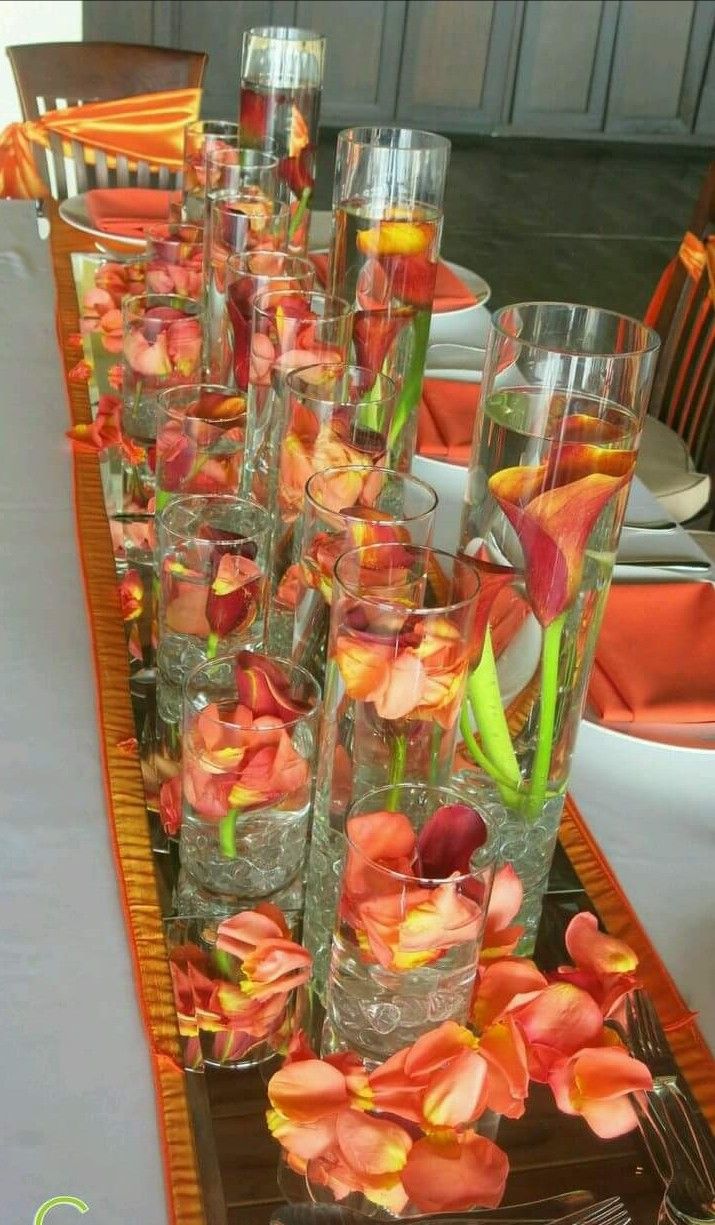 there are many glasses with flowers in them on the long table, along with plates and utensils