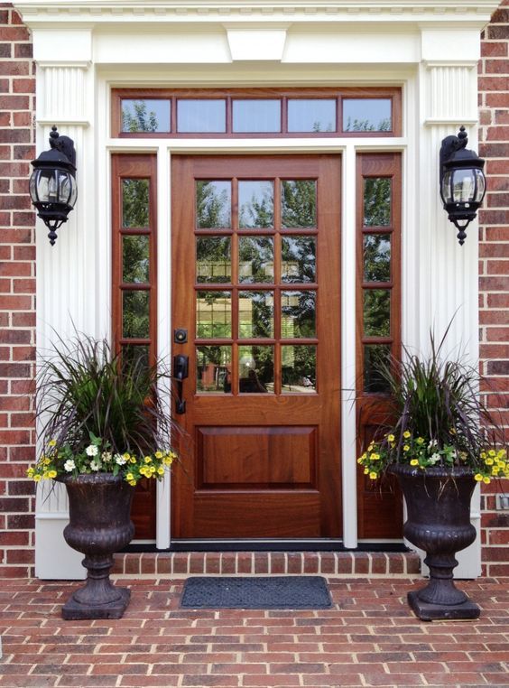 two large planters with flowers are in front of a wooden door on a brick building