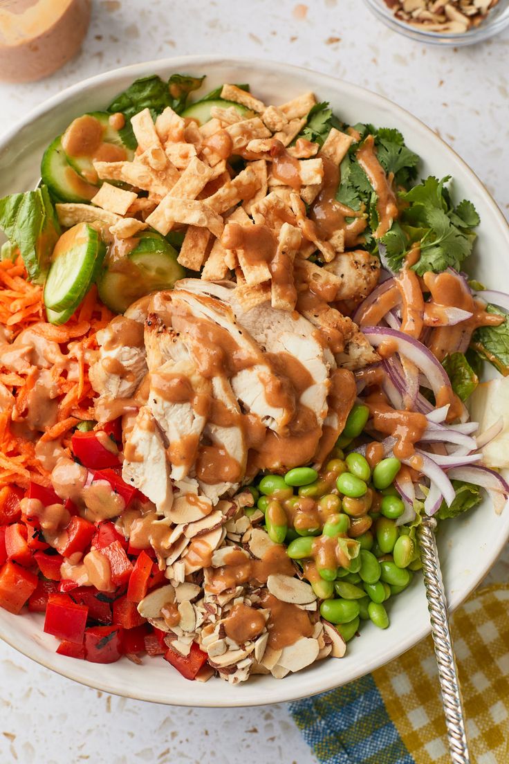 a salad with chicken, carrots, and green beans in a white bowl on a checkered table cloth