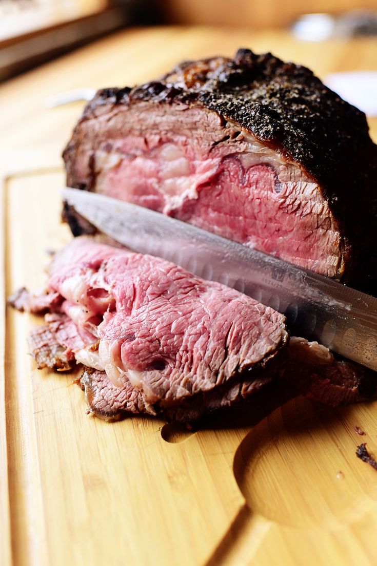 a large piece of meat is being sliced on a cutting board with a knife in it