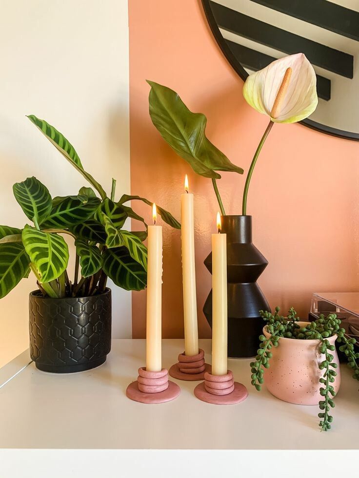 three candles are sitting on a table next to some potted plants and a mirror