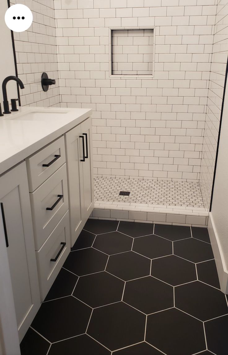 a bathroom with black and white hexagonal floor tiles on the shower wall, vanity sink, and toilet